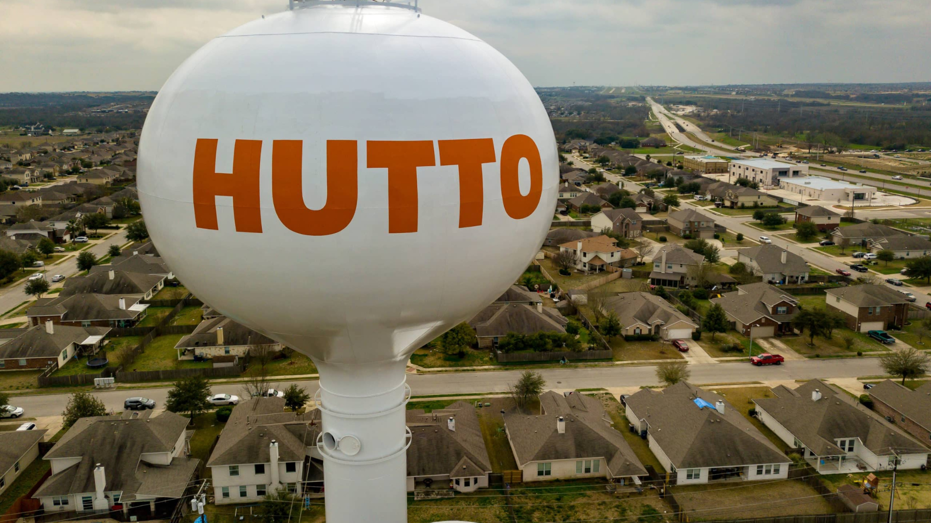 Aerial view of the Round Rock water tower in Texas, overlooking the downtown area with buildings, streets, and lush greenery during sunset.