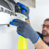 A cleaning wearing blue gloves is cleaning an air conditioner unit with a spray bottle. This image highlights our affordable cleaning service in Round Rock, TX, where we provide expert cleaning for air conditioning systems, ensuring efficiency and cleanliness for a healthier home or office. Learn more in our blog post, 'Top 10 Reasons to Hire a Cleaning Service in Round Rock, TX.