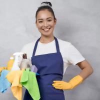 A smiling professional cleaner in yellow gloves and a blue apron holds a caddy filled with cleaning supplies. This image represents our maid service in Georgetown, TX, offering reliable and friendly cleaning solutions for both residential and commercial needs.